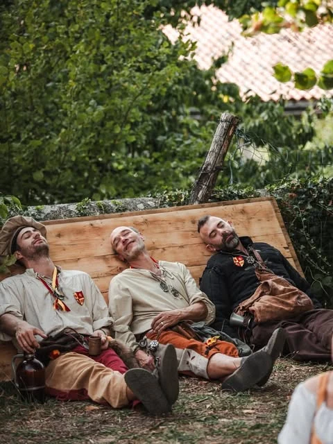 Trois compagnons costumés font une pause au pied des arbres, contre un panneau en bois